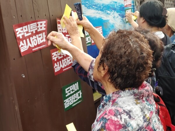 제주도청 벽에 주민투표 실시를 촉구하는 스티커를 붙이고 있는 제2공항 피해지역 주민들.(사진=김재훈 기자)