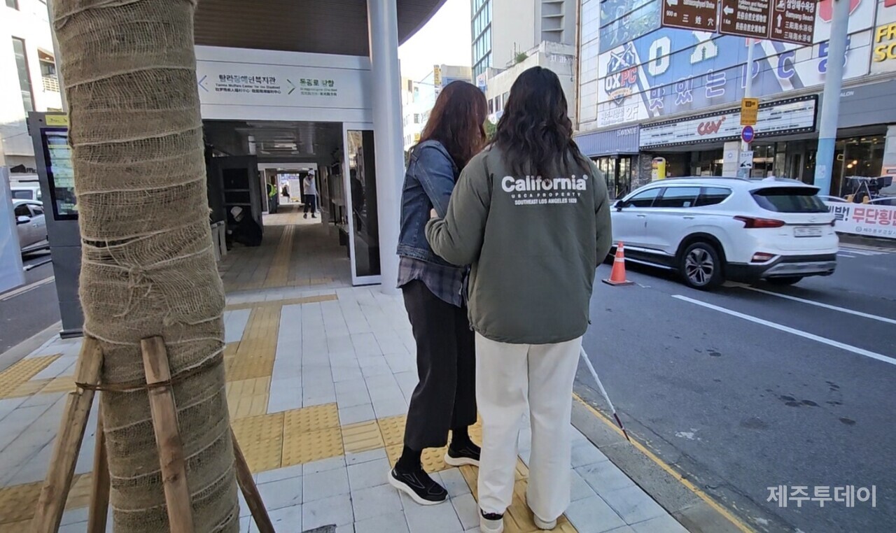 시각장애가 있는 문채영 활동가와 근로지원인. 섬식정류장에 심어놓은 중앙의 나무를 피해 이동하면서 차도로 떨어질 수 있는 위험이 있다.(사진=김재훈 기자)